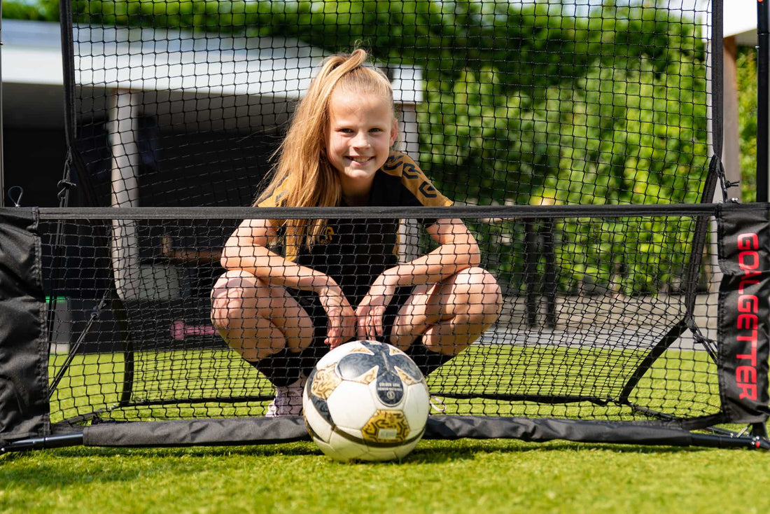 Young girl practicing football with a rebounder at home. Perfect backyard football training setup for kids.