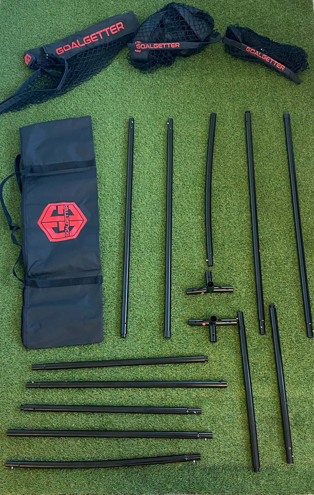 Multifunctional football training gear laid out on artificial grass, including black metal poles, netting with 'Goalgetter' branding, connectors, and a carrying bag. Ideal for agility, shooting, and skill development drills